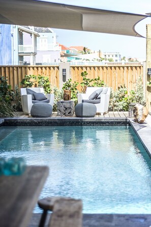 A pool area with two white chairs and a small table, surrounded by a wooden fence and greenery. - Pietermaai Ocean Front (Willemstad)