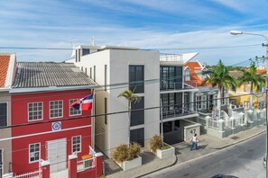 A street view with a red building, a white building, and a modern structure with balconies. - Pietermaai Ocean Front (Willemstad)