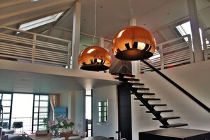 A modern interior with a staircase, large windows, and hanging pendant lights. - Pietermaai Ocean Front (Willemstad)