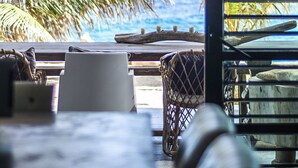 A view of a beachside lounge with a table and chairs, palm trees, and a view of the ocean. - Pietermaai Ocean Front (Willemstad)