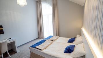 Quarto de hotel com uma cama, uma escrivaninha e uma televisão.
