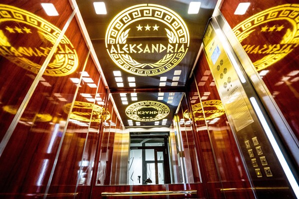 Interior de un ascensor con un logotipo circular y el texto que dice "ALEXANDRIA" y "ALEXANDRIA HOTEL".
