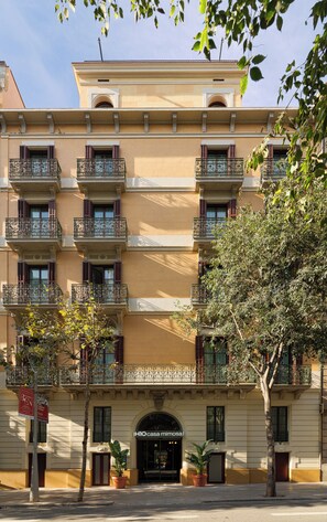 A multi-story building with balconies, a central entrance, and potted plants. - H10 Casa Mimosa (Barcelona)