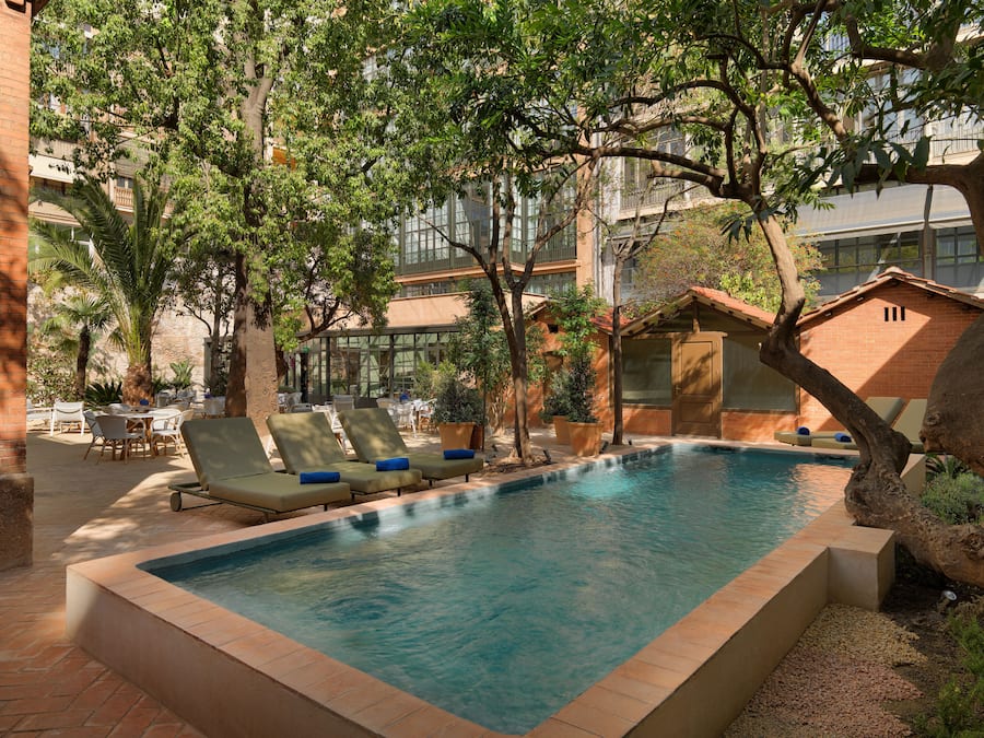 Un área de piscina con sillones reclinables, una piscina pequeña y follaje circundante.