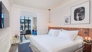 A hotel room with a large bed, a TV, a desk with a chair, and a view of the city through the window.