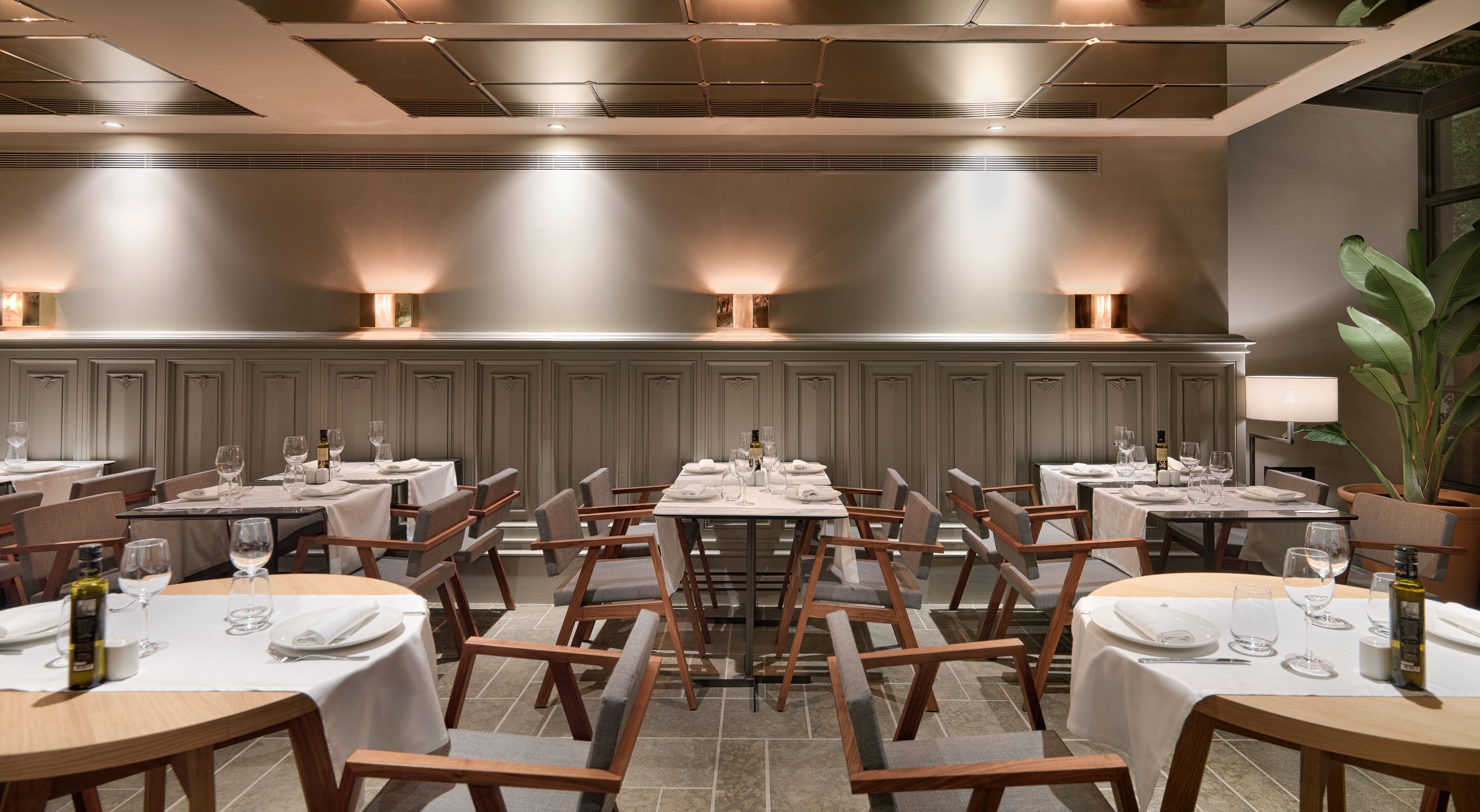 Un restaurante con varias mesas, cada una con mantel blanco, sillas y copas de vino.