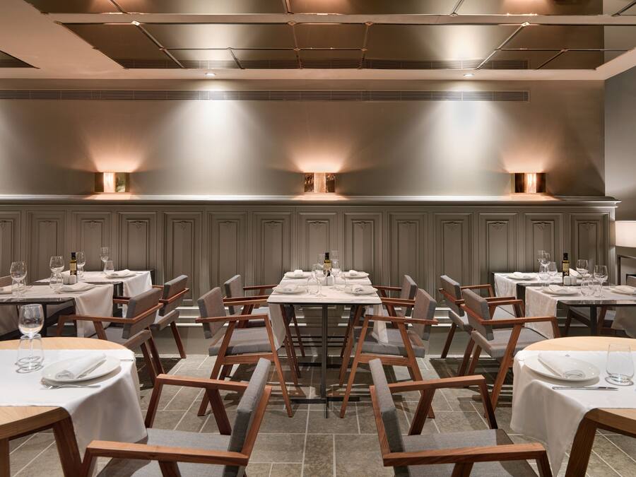 Un restaurante con varias mesas, cada una con mantel blanco, sillas y copas de vino.
