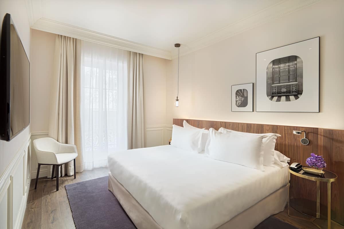 A hotel room with a large bed, a chair, a nightstand with a lamp, and two framed pictures on the wall.