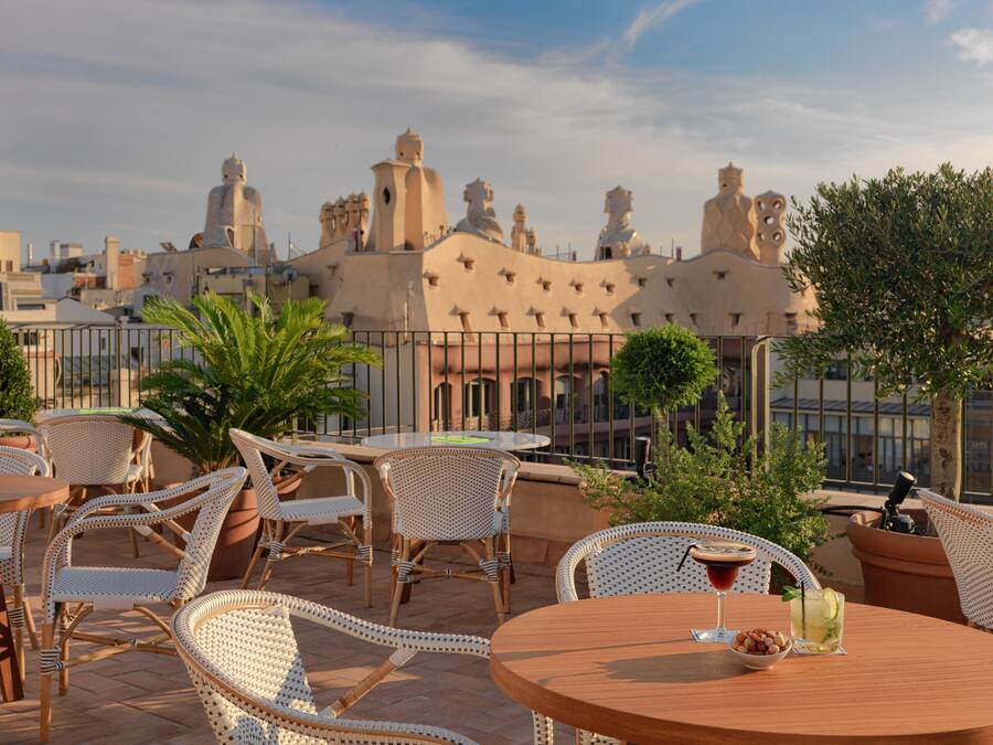 A rooftop terrace with wicker furniture and a round table, overlooking a cityscape with distinctive architecture.