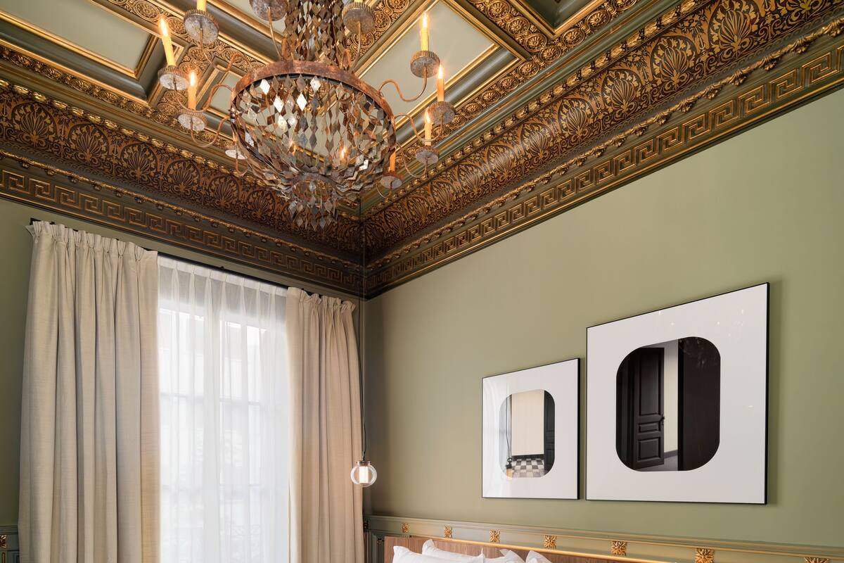 A spacious bedroom with a large bed, a chandelier, and ornate ceiling details.