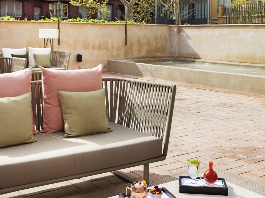 An outdoor seating area with a sofa, cushions, and a tray with food and drinks.