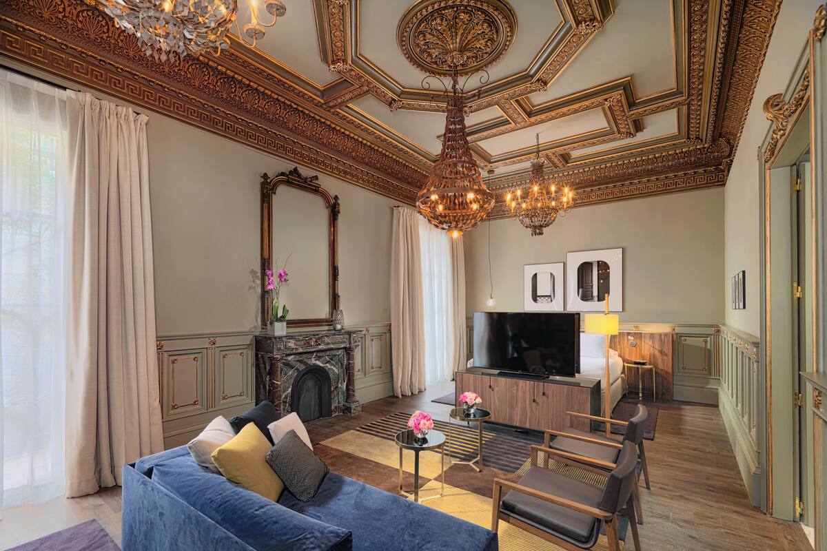 A luxurious living room with a blue sofa, a fireplace, a TV, and a chandelier.
