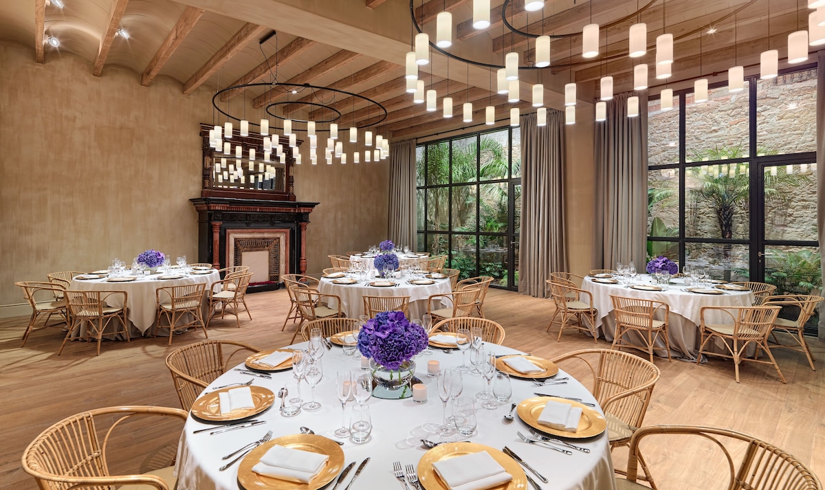 A spacious dining area with round tables, wicker chairs, and a fireplace.