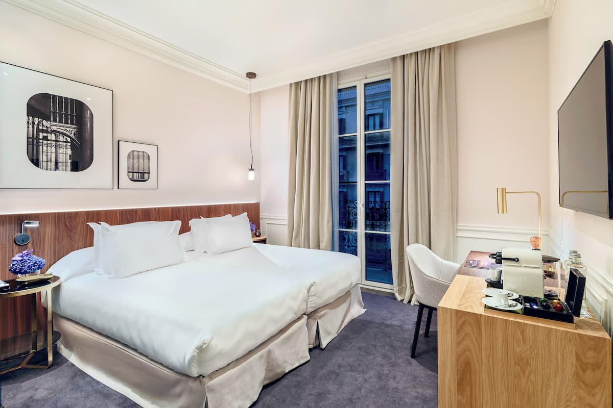 A hotel room with a large bed, a desk with a chair, a TV, and a window with curtains.
