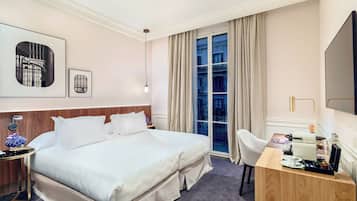A hotel room with a large bed, a desk with a chair, a TV, and a window with curtains.