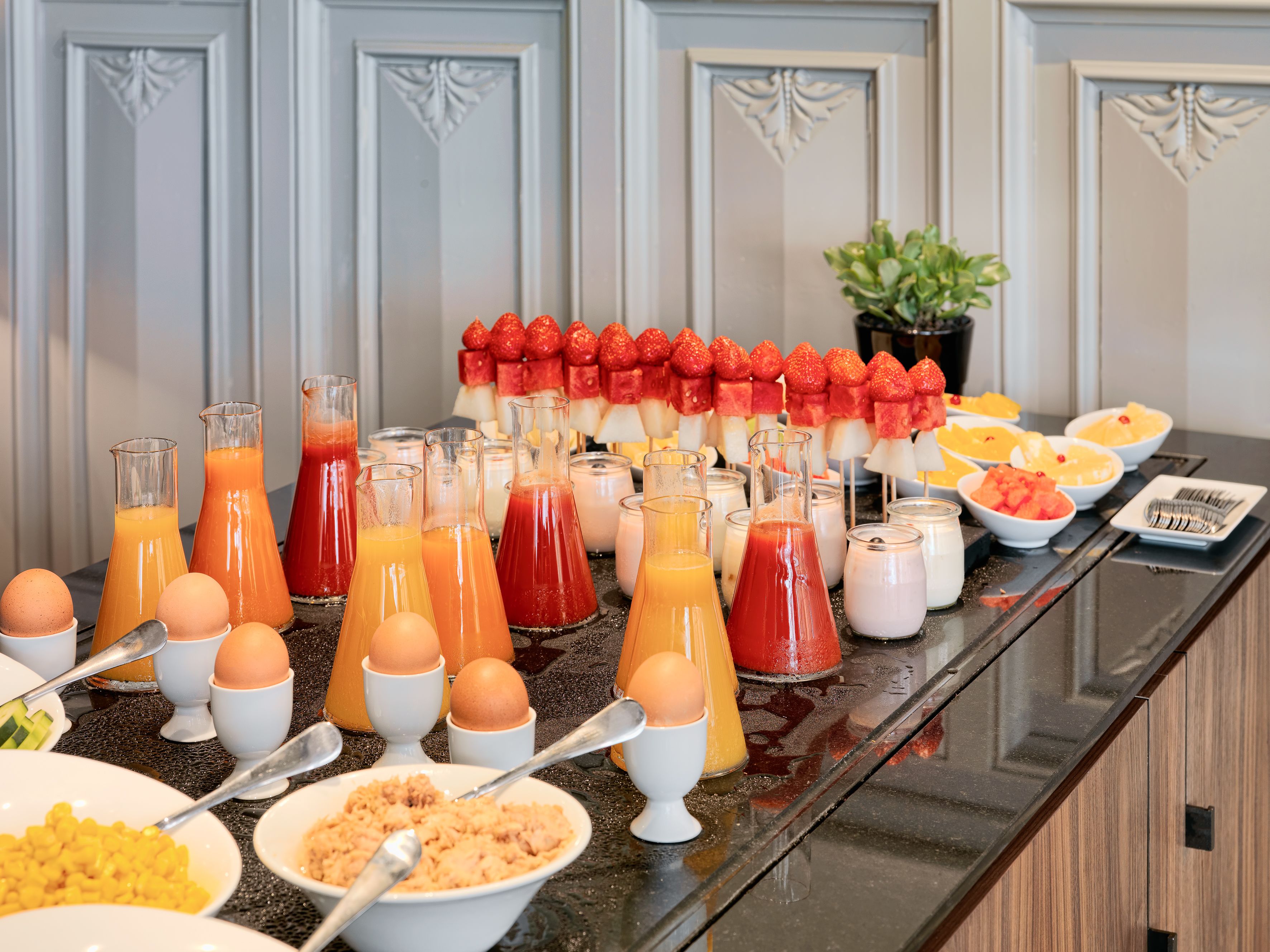 Un bufé de desayuno con varios jugos, huevos y brochetas de fruta.