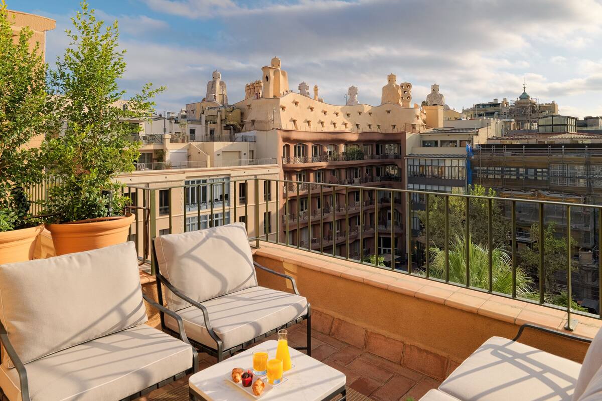 A rooftop terrace with outdoor seating, a table with breakfast items, and a view of the cityscape.