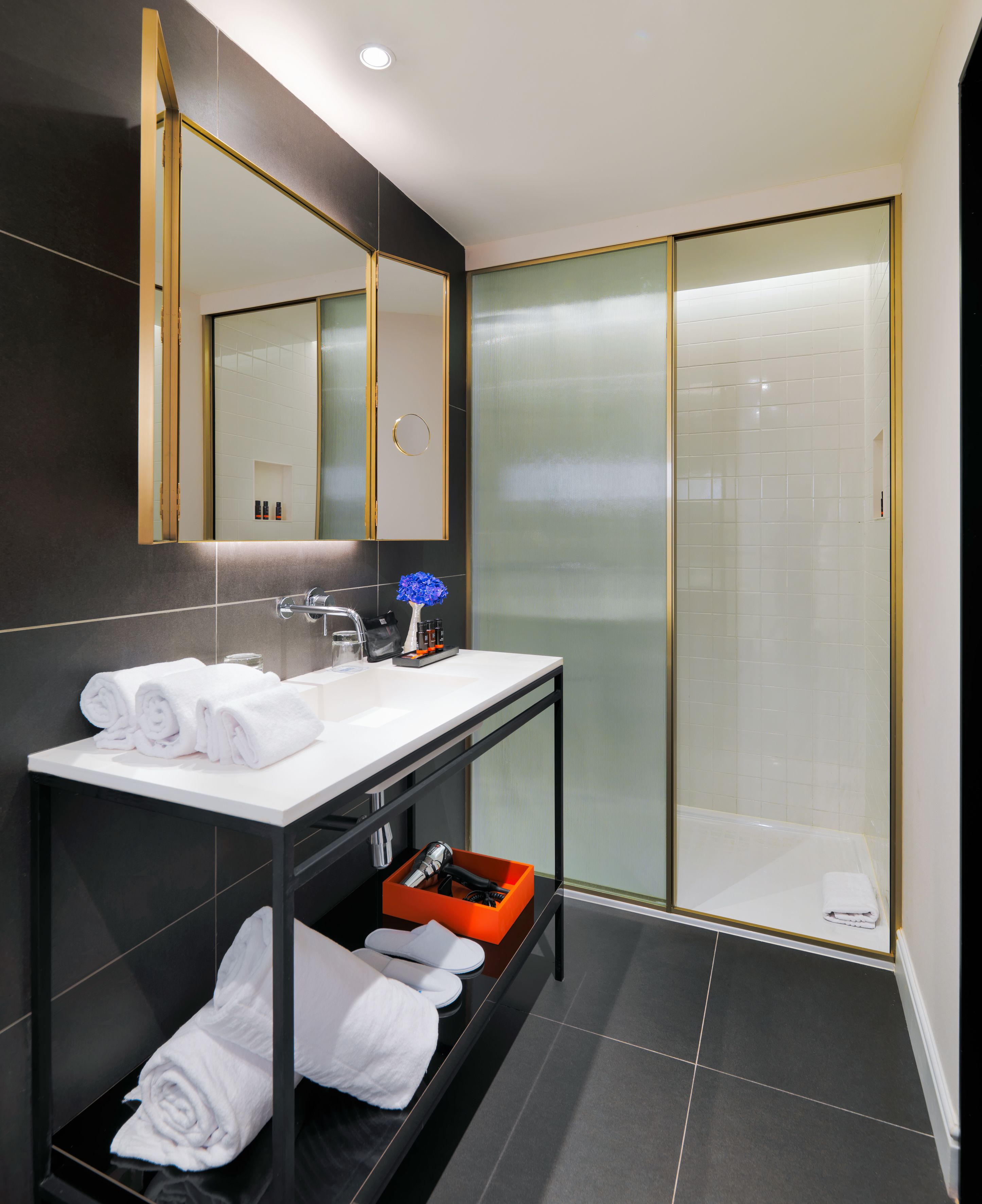 Un baño moderno con un espejo grande, lavamanos blanco y cabina de ducha de vidrio.