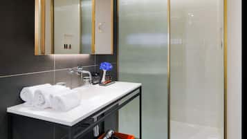 Un baño moderno con un espejo grande, lavamanos blanco y cabina de ducha de vidrio.