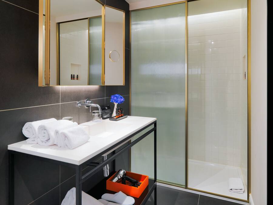 Un baño moderno con un espejo grande, lavamanos blanco y cabina de ducha de vidrio.