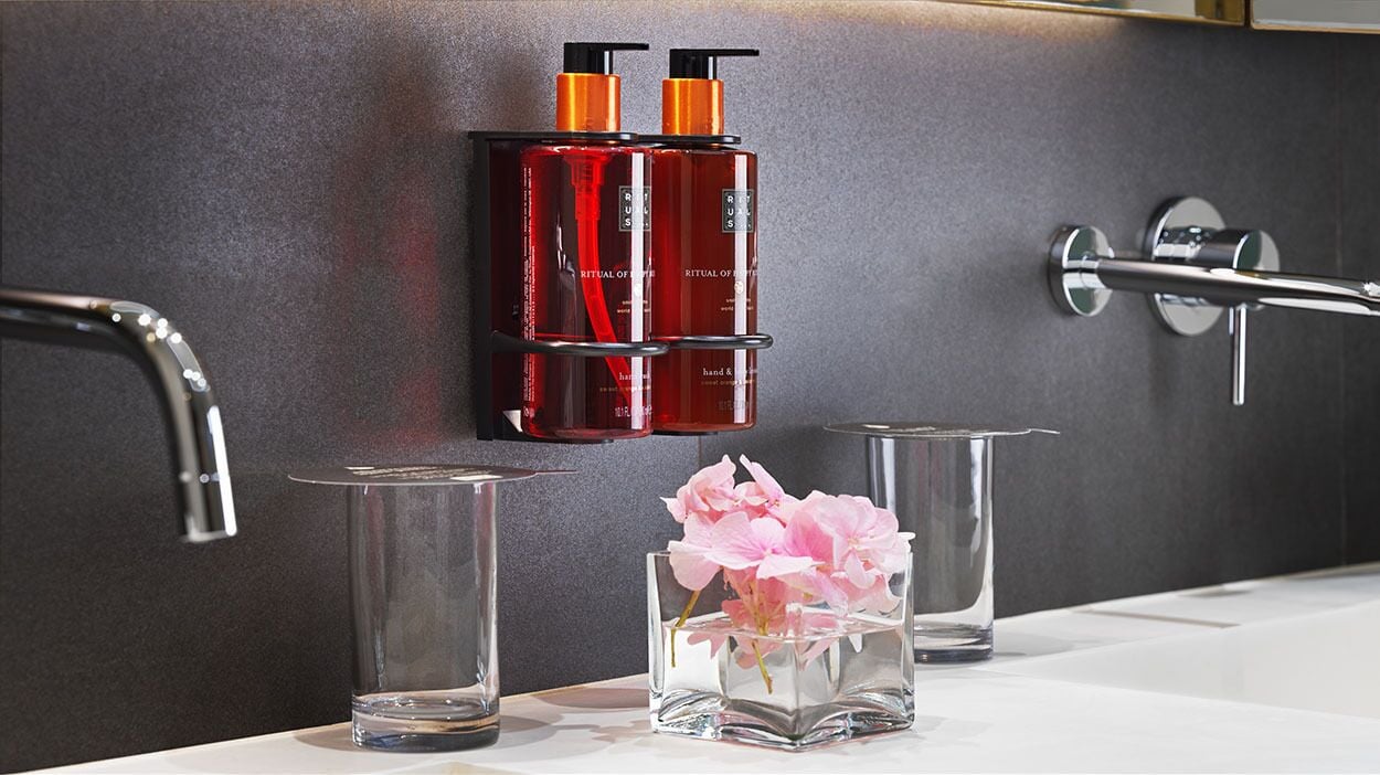 Ein modernes Badezimmer mit Wandseifenspender und einer Glasvase mit rosa Blumen.