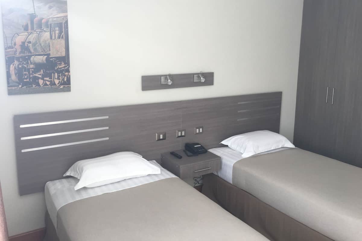 Ein Hotelzimmer mit zwei Einzelbetten, einem Nachttisch mit Telefon, einem kleinen Tisch und einem Kleiderschrank.