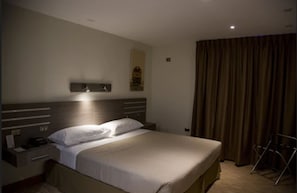 A hotel room with a large bed, a nightstand, a lamp, a curtain, and a small table. - Hotel Alto del Sol Plaza Mejillones (Mejillones)