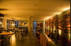 A restaurant with a long counter, multiple tables, and a wall with stacked books. - Hotel Alto del Sol Plaza Mejillones (Mejillones)