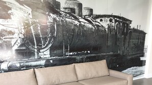 A modern living room with a beige sofa, a round wooden coffee table with potted plants, and a large abstract painting on the wall.