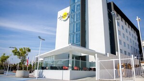 A modern hotel with a prominent logo, a covered outdoor seating area, and a gated entrance.