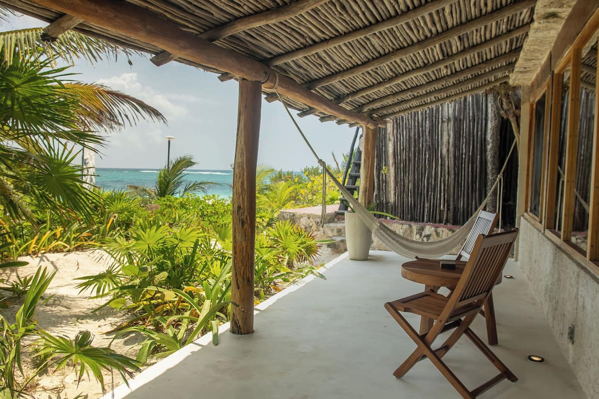 A beachside patio with a hammock, wooden chairs, and a view of the ocean.