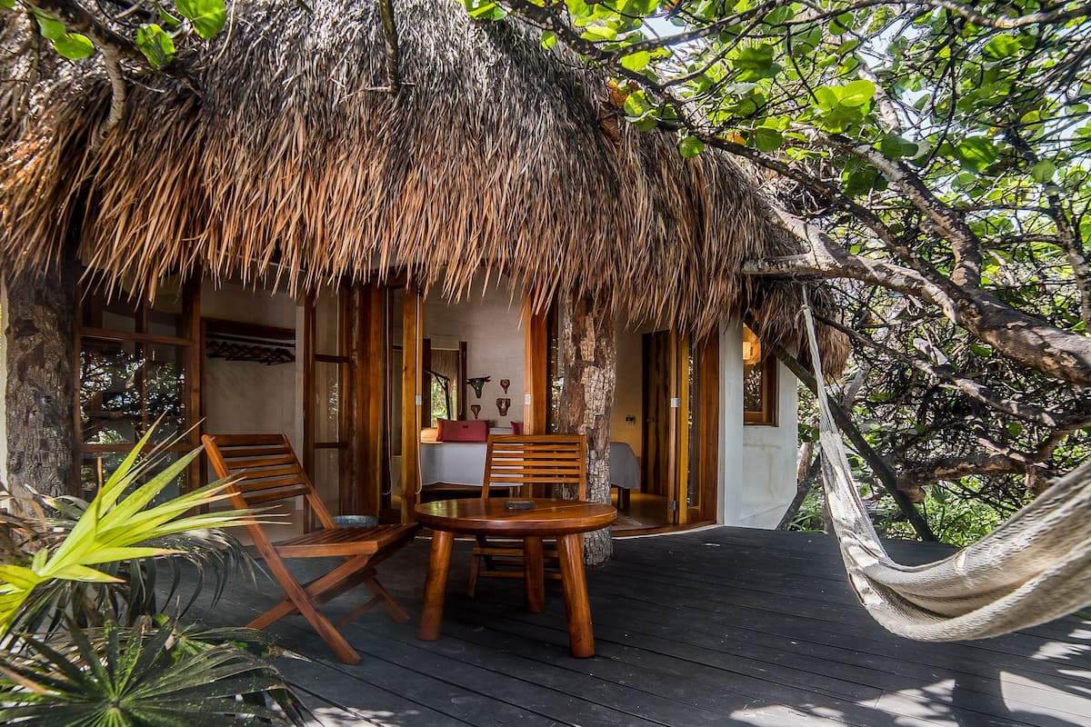 A thatched-roof structure with a wooden deck, a dining table, and two chairs.
