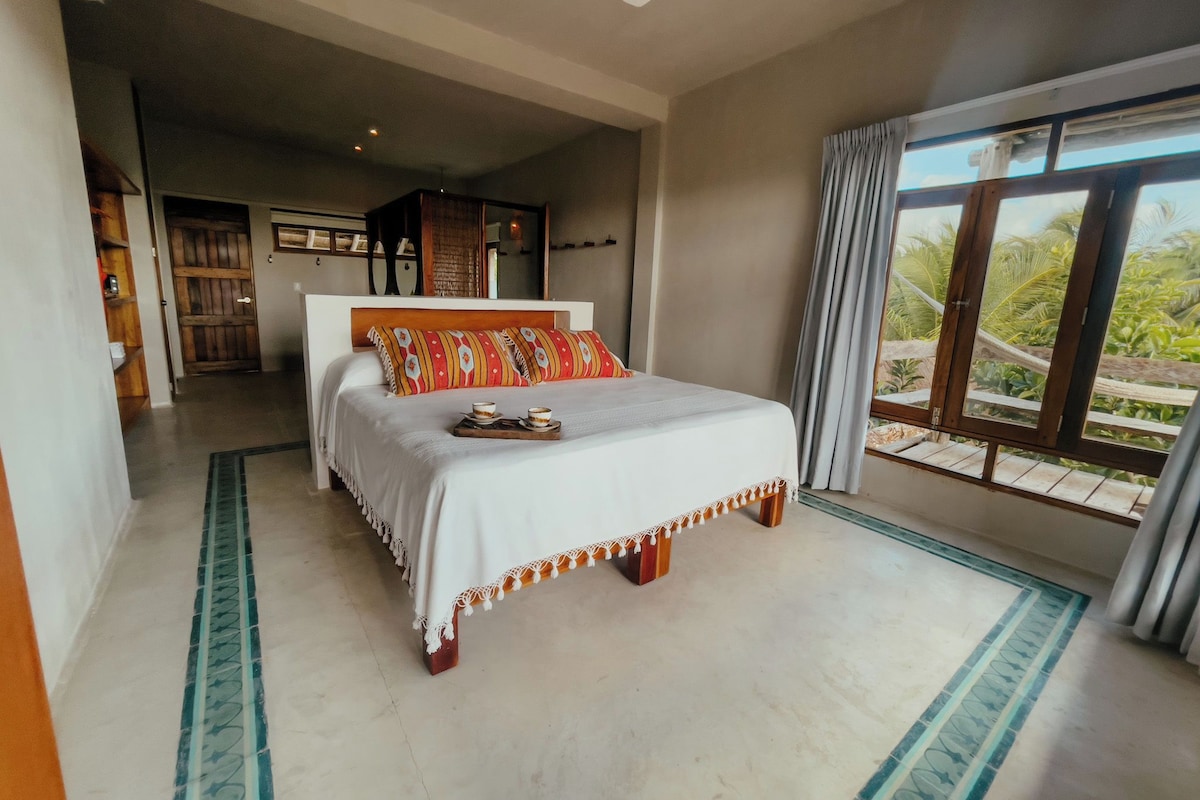 A spacious bedroom with a large bed, a ceiling fan, and a view of the outdoors through a large window.