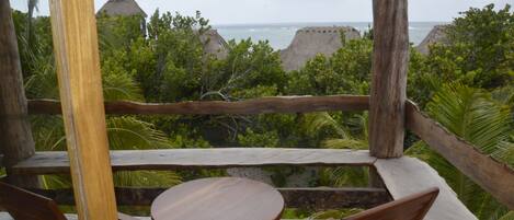 A wooden deck with a table and chairs, overlooking a lush landscape with trees and a view of the ocean.