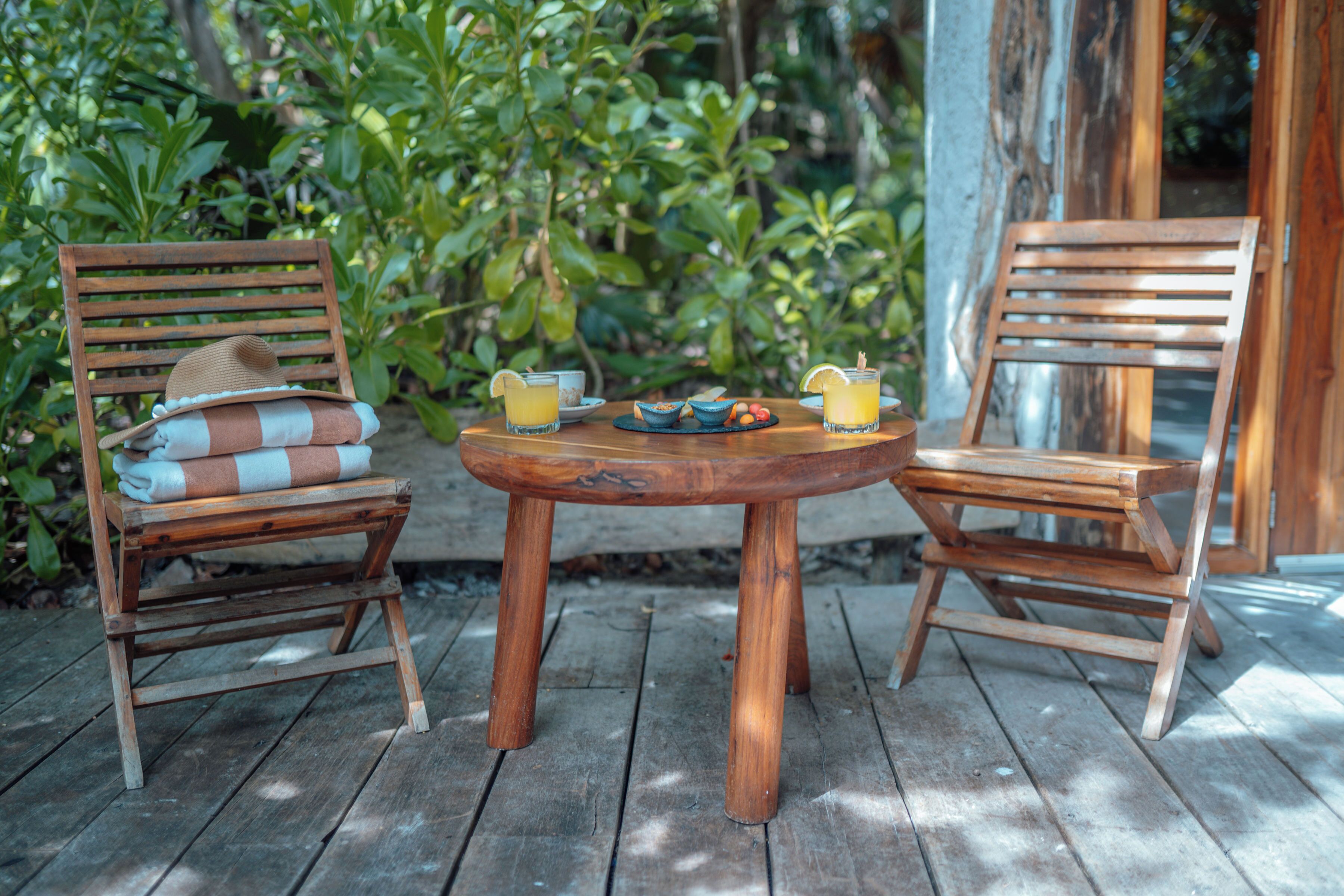 A wooden table with two chairs, each with a hat and a folded towel. There are two drinks on the table.