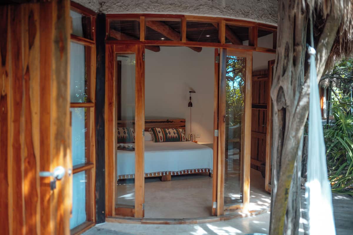 A room with a bed, wooden door, and a view of the outdoors.