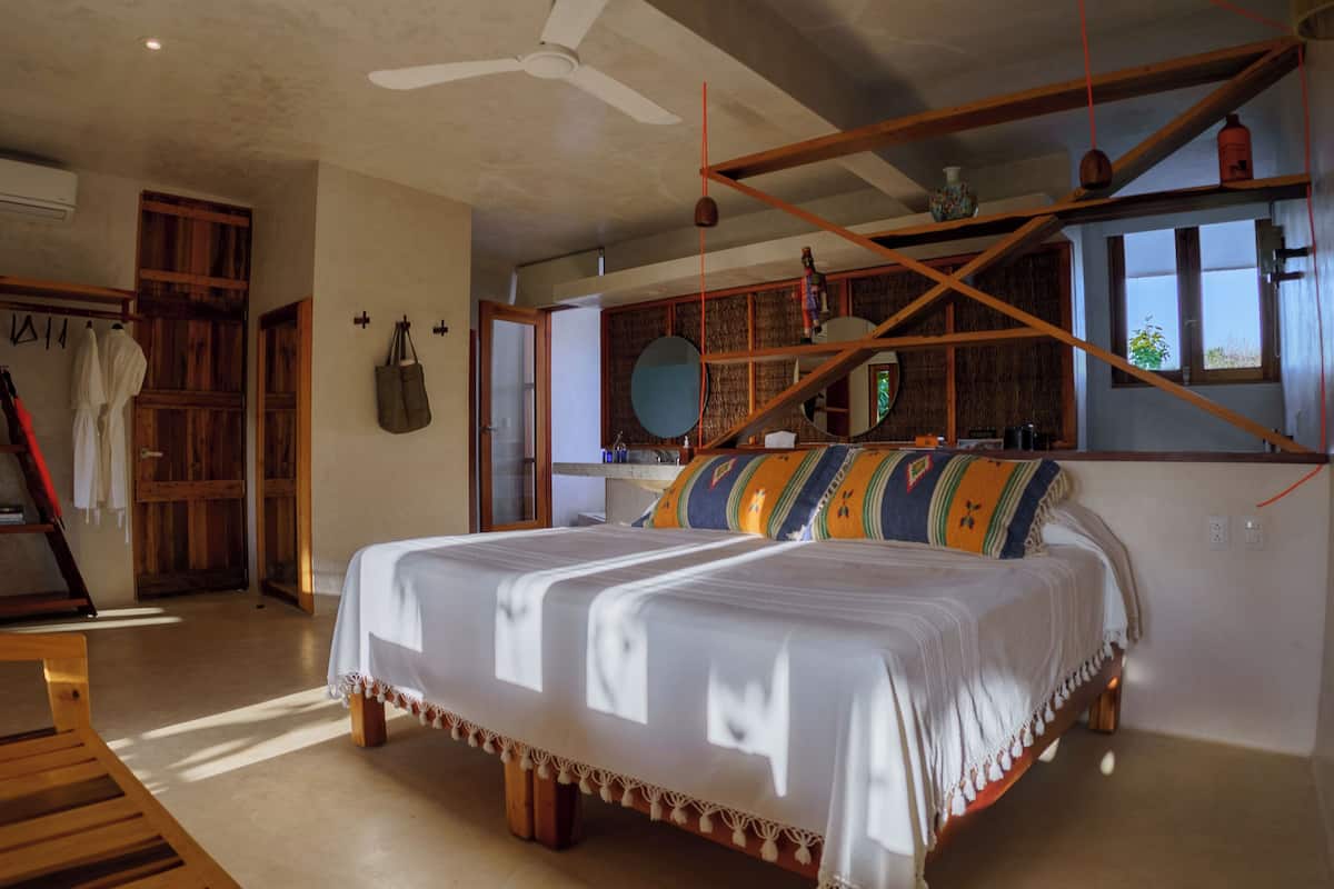 A bedroom with a large bed, wooden beams, a ceiling fan, and a window with a view.