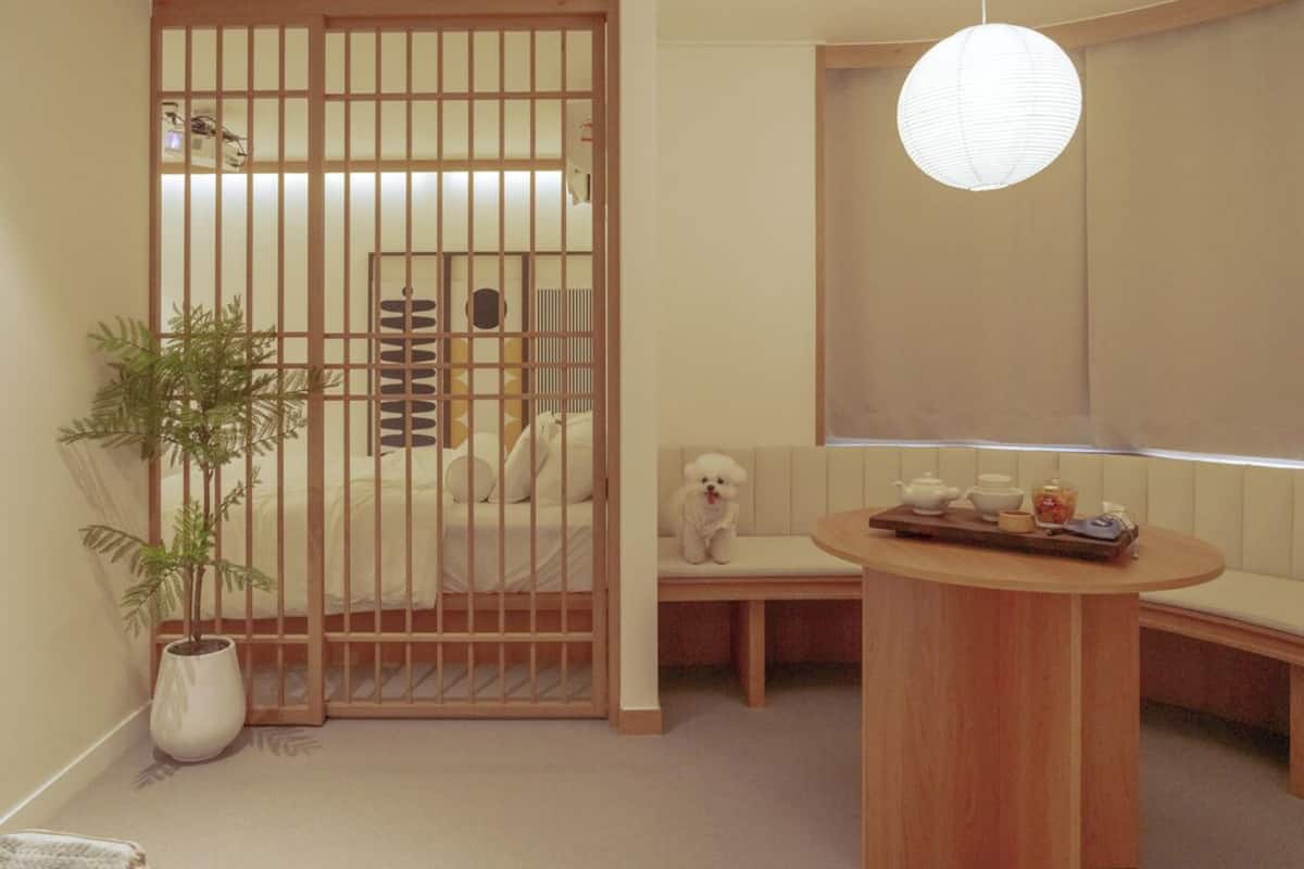 A room with a sliding door, a small round table with tea set, a sofa, a potted plant, and a hanging light fixture.