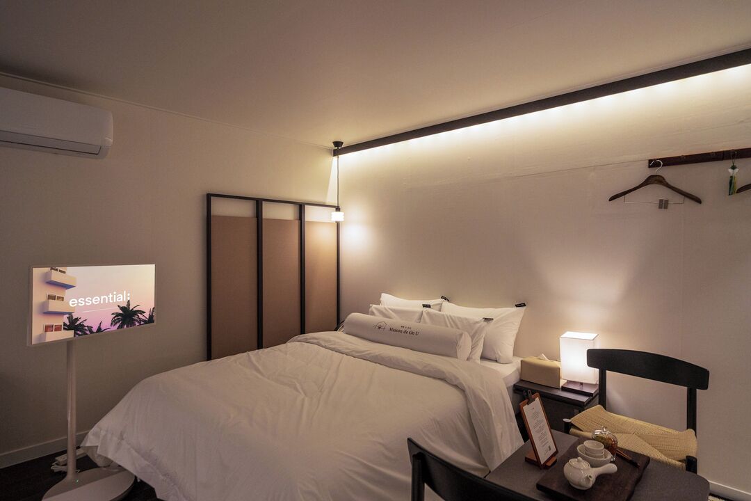 A hotel room with a bed, bedside table, lamp, and a wall-mounted air conditioner.