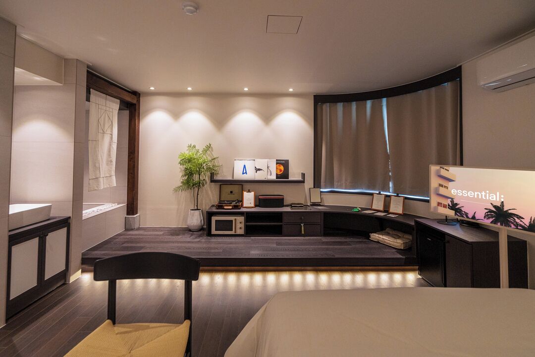 Une chambre d’hôtel moderne équipée d’un lit, d’un bureau, d’une télévision, d’une plante et d’une fenêtre avec des rideaux.