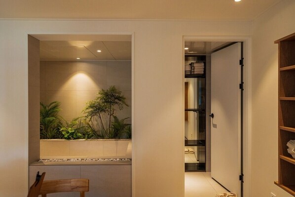 A hallway with a wooden bench, a tiled wall with a plant, and a door leading to a room with a bed. - Maison de On U Jeonju Hanok Village (Jeonju)