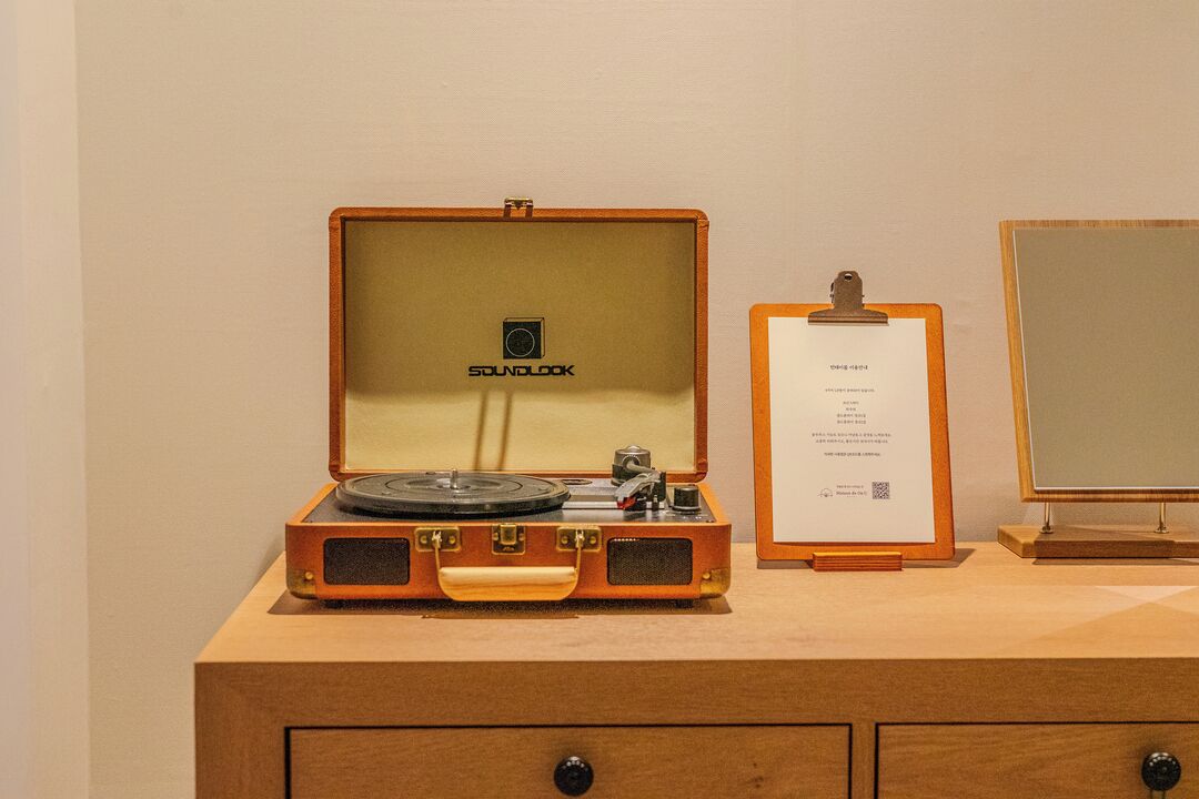 A vintage record player in a wooden case with a label, a framed certificate, and a mirror on a wooden dresser.