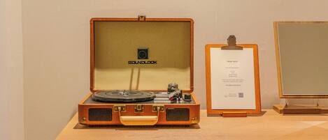 A vintage record player in a wooden case with a label, a framed certificate, and a mirror on a wooden dresser.