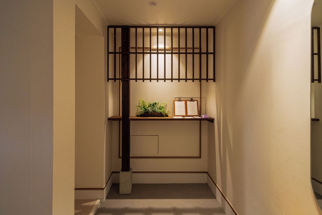 A narrow hallway with a wooden partition, a small shelf with plants, and a bulletin board.