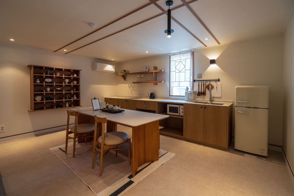 A modern kitchen with wooden cabinets, a dining table with chairs, a built-in oven, and a refrigerator.