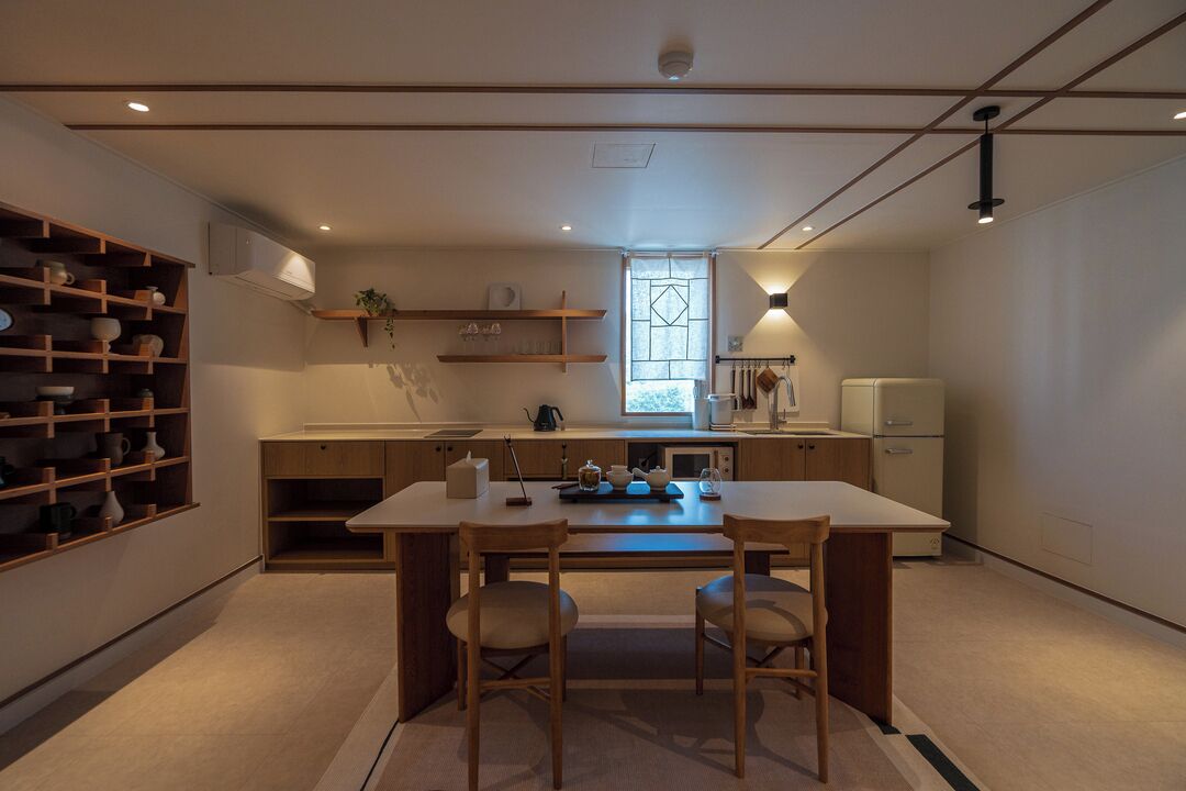 A modern kitchen with a central island, wooden chairs, and built-in shelves.