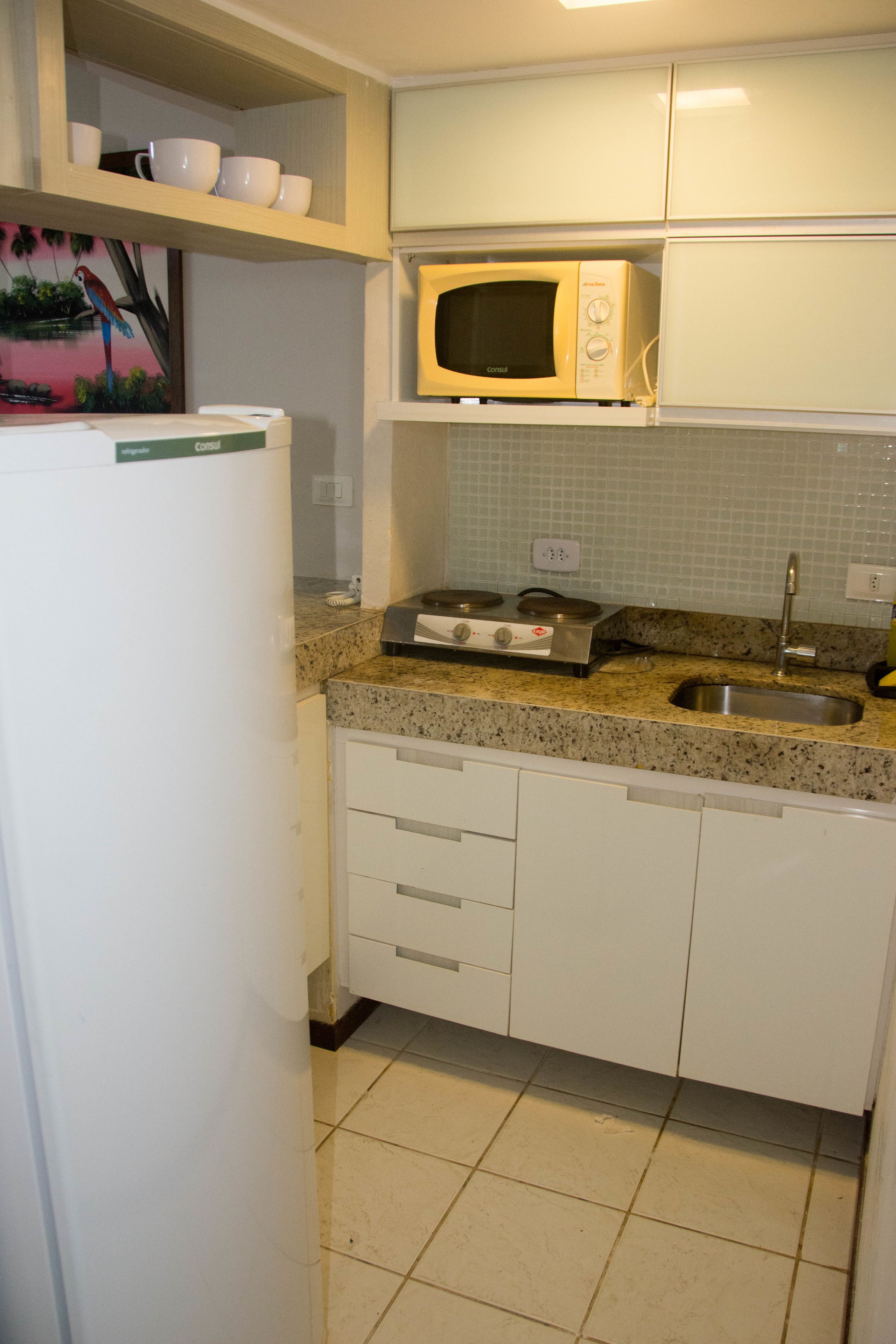 Cozinha com micro-ondas, fogão, pia e armários brancos.
