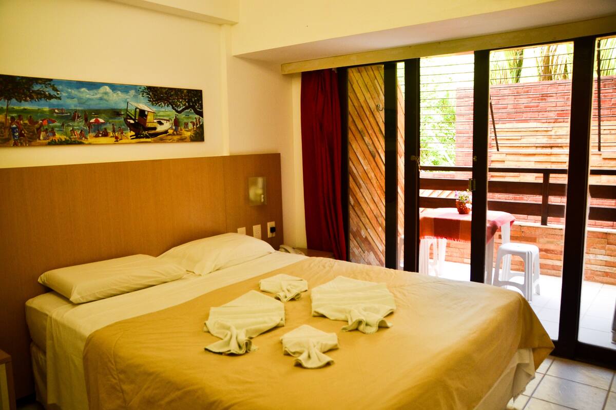 A hotel room with a bed, a painting on the wall, and a view of the outside.