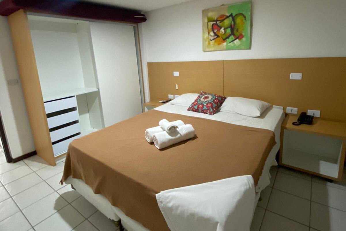 A hotel room with a bed, a nightstand, a telephone, and a painting on the wall.