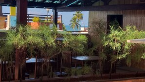 An outdoor seating area with wooden tables and chairs, surrounded by lush greenery and a view of the ocean. - Flat Pipa Oceano (Tibau do Sul)